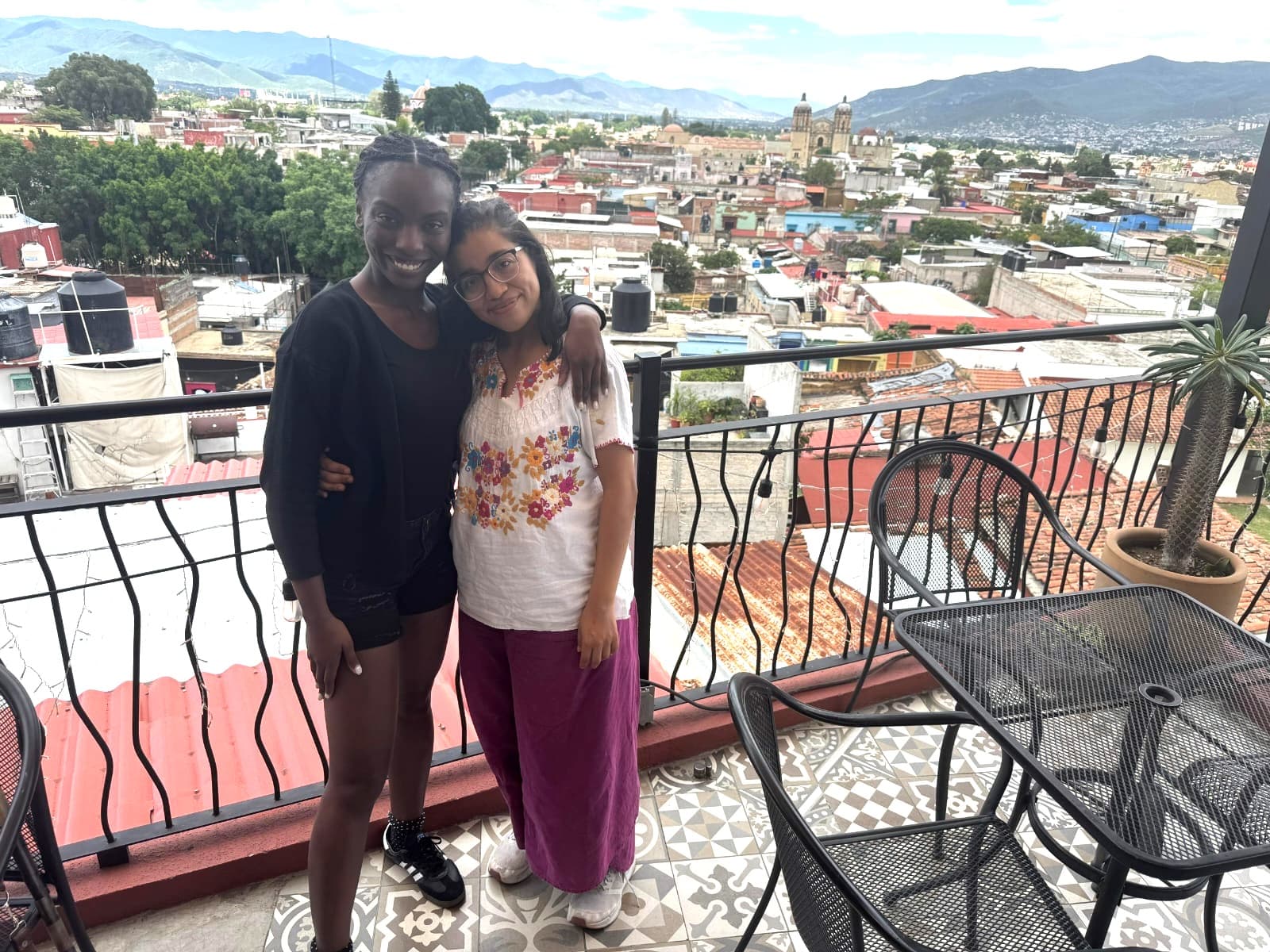 Spanish teacher and student posing together on a rooftop terrace overlooking the Oaxaca cityscape and mountains